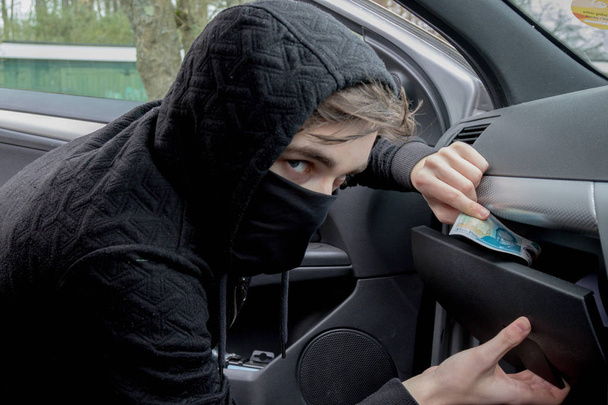 Masked teenage criminal stealing from a car - Foto, Bild