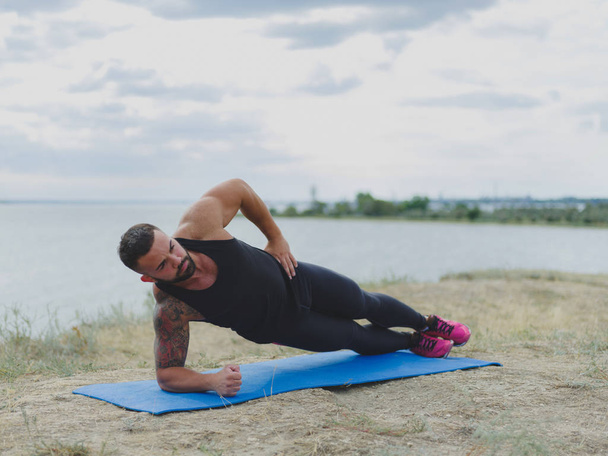 An athletic, strong man with a muscular body doing exercises on a mat on a natural background. Fitness, sports concept. - Фото, зображення