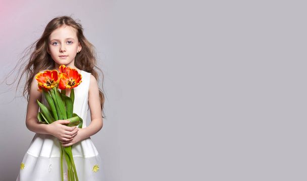Fashion red-haired girl with tulips in hands. Studio photo on light coloured background. Birthday, holiday, mother's day, first day of school - Photo, Image
