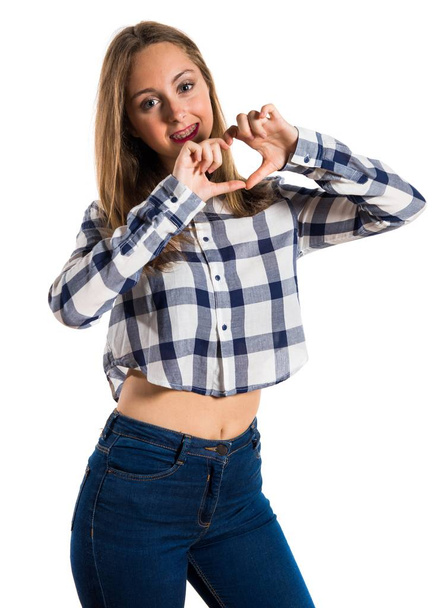 Blonde teen girl making a heart with her hands on textured backg - Foto, afbeelding