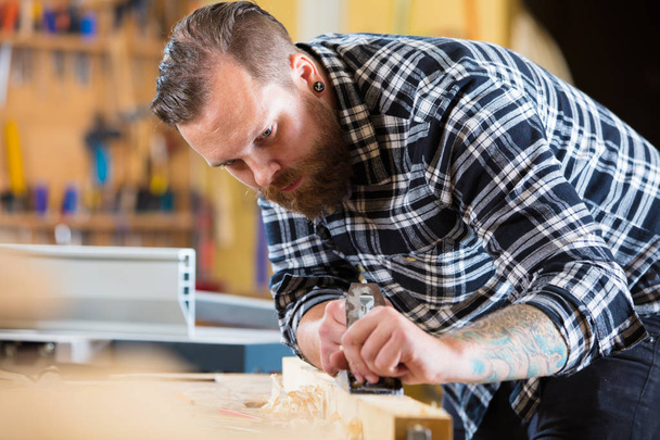 Tischler arbeitet in Werkstatt mit Hobel auf Holzplanke - Foto, Bild