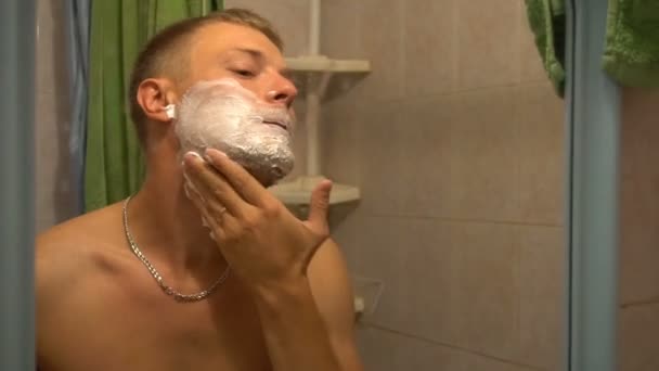 the young man rubs his face with shaving cream - Filmati, video
