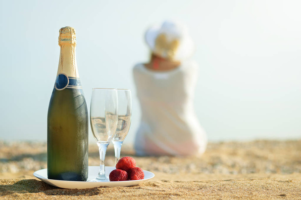 Bessen verse aardbeien, fles champagne, bril en de vrouw op het strand. - Foto, afbeelding