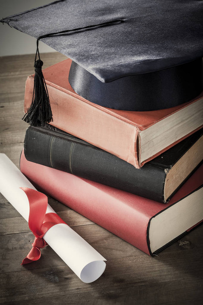 Chapéu de graduação e diploma com livro na mesa
 - Foto, Imagem