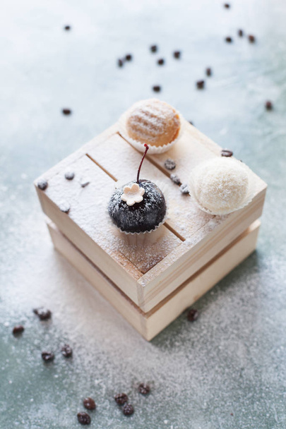 cakes on a light wooden box with coffee beans on a blue background sprinkled with powdered sugar - Photo, image