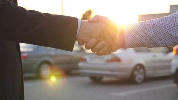 Business handshake outdoor at sunset. Two businessmen greeting each other at the car parking. Shaking of male arms outside. Colleagues meet and shake hands in the city background. Close up Slow motion - Footage, Video