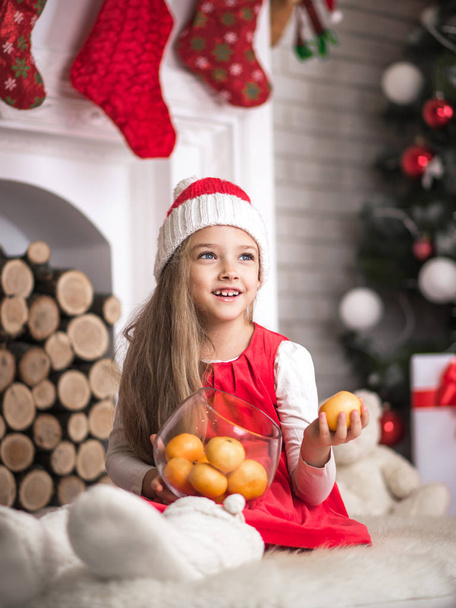 Lovely girl in santa cap with tangerines in hand, studio shot. - Photo, image