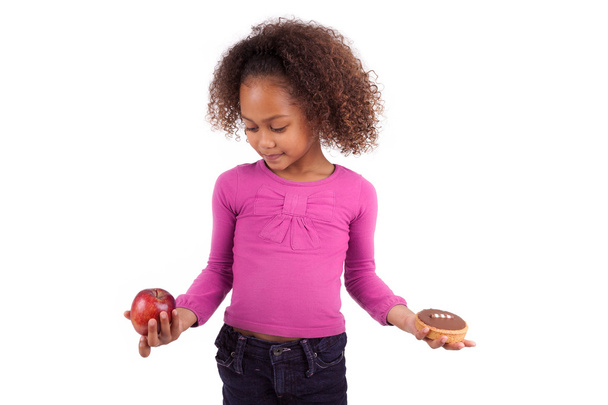Little African Asian girl hesitating between fruits or candy - Foto, afbeelding