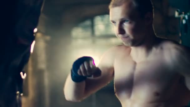 Muscular Shirtless Man Hits Punching Bag with His Fists. Part of His Gym Training. - Filmmaterial, Video