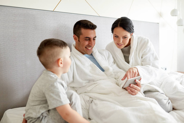happy family with smartphone in bed at hotel room - Foto, Bild