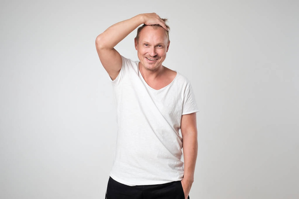 Jeune homme souriant en t-shirt blanc debout sur fond blanc Concept d'homme confiant en soi
. - Photo, image