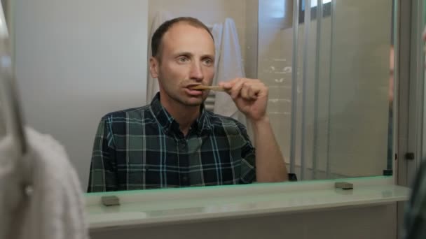 Young man brushing teeth while standing in bathroom indoors. - Imágenes, Vídeo