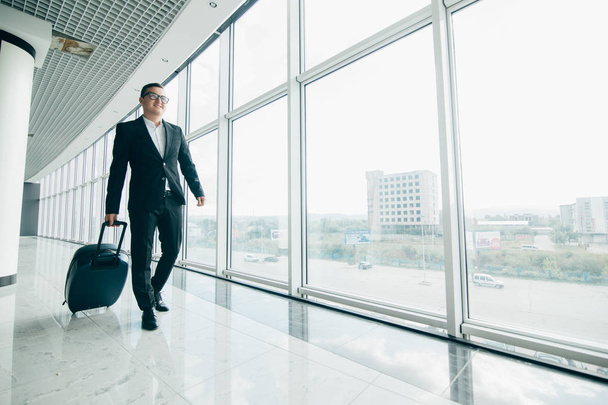 Ο επιχειρηματίας με τα πόδια με μια βαλίτσα κοντά σε παράθυρα με πανοραμική θέα στο αεροδρόμιο - Φωτογραφία, εικόνα