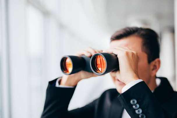Hombre de negocios mirando con prismáticos sobre ventanas panorámicas
 - Foto, Imagen