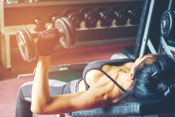 Asian sports woman doing exercises with dumbbell weights in gym - Foto, imagen