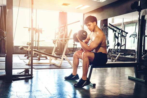 Muscular Man atleta construido haciendo ejercicio en el gimnasio sentado en el peso
 - Foto, Imagen