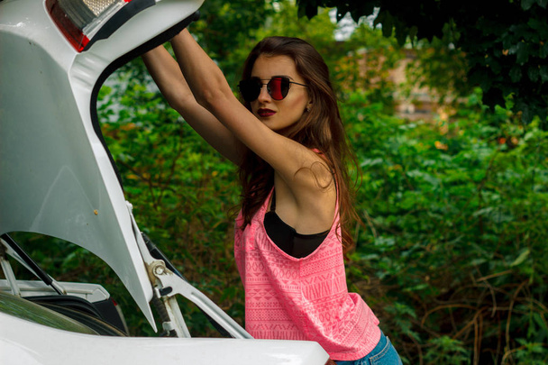 beautiful lady in a bright t-shirt and glasses opens the hood - Photo, Image