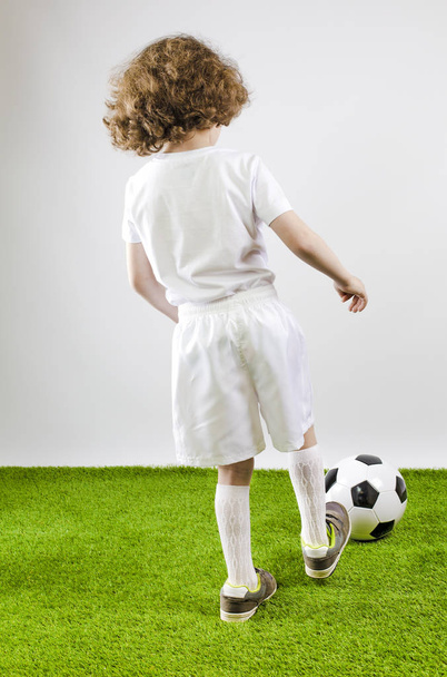 Boy with soccer ball on a gray background. Back view - Zdjęcie, obraz