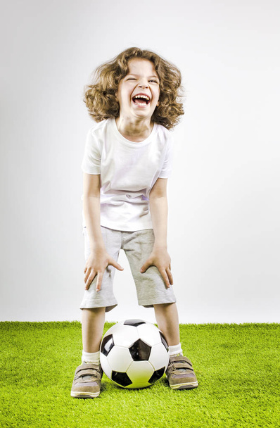 Mały chłopiec w białe szorty i białą koszulę, grając z piłki nożnej. Zabawny chłopak śmieje się na głos. - Zdjęcie, obraz