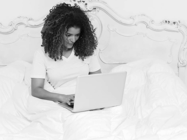 Beautiful girl portrait sitting in bed under blankets and using laptop, monochrome - Fotoğraf, Görsel
