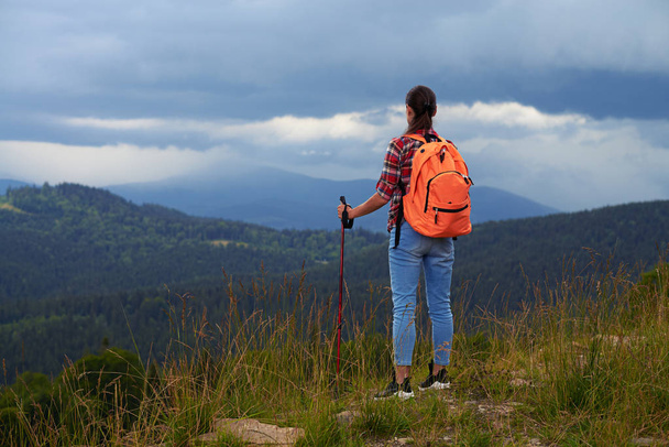 Femake hiker standing with backpack and poles on the mountain  - Photo, Image