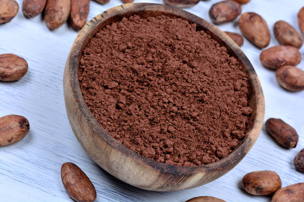 Kom met cacaopoeder en bonen op tafel - Foto, afbeelding