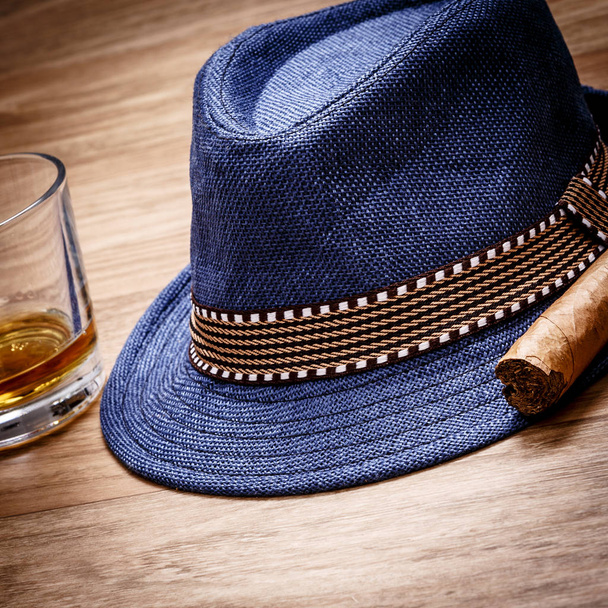 blue hat with cigar and expensive drink of whisky or rum on wooden floor - Photo, Image