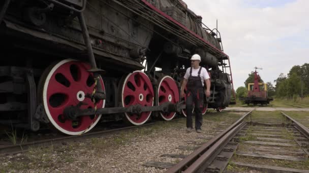 Železniční zaměstnanec pěší poblíž lokomotiva na kolejích - Záběry, video