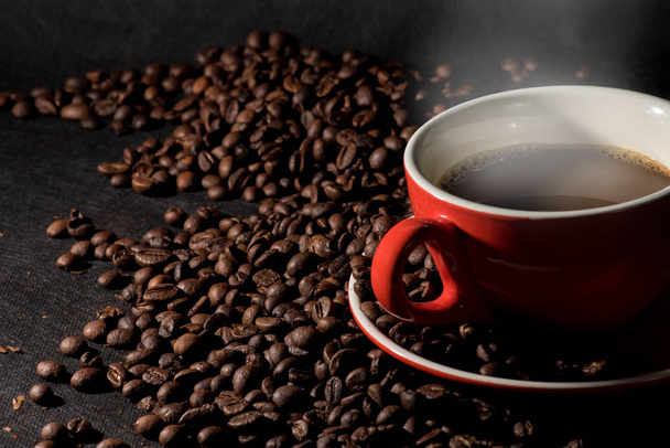 Warme koffie in rode kop en koffiebonen zijn de achtergrond. - Foto, afbeelding