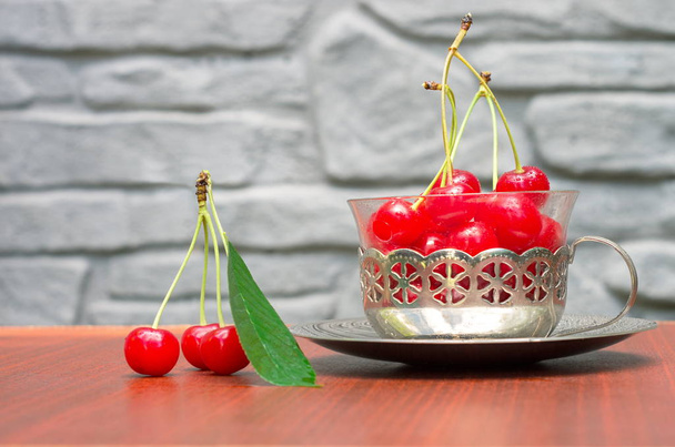 Cerezas rojas maduras con esquejes en una taza con un borde de hierro en la mesa
 - Foto, Imagen