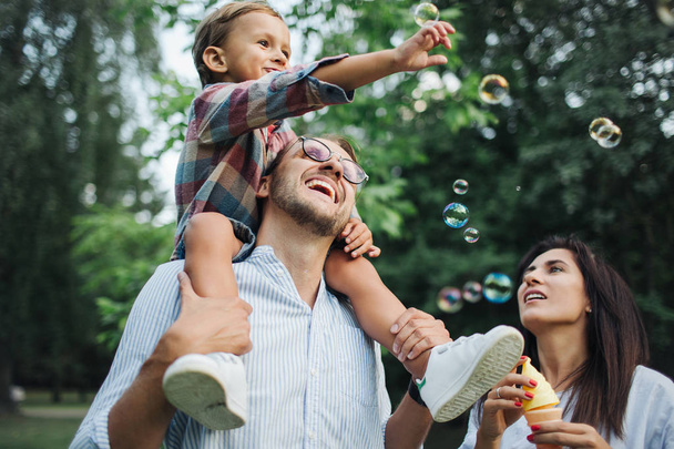 Happy young family playing with bubble wands in park outdoors - 写真・画像