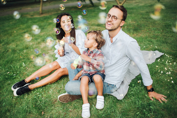 Happy young family playing with bubble wands in park outdoors - Foto, imagen
