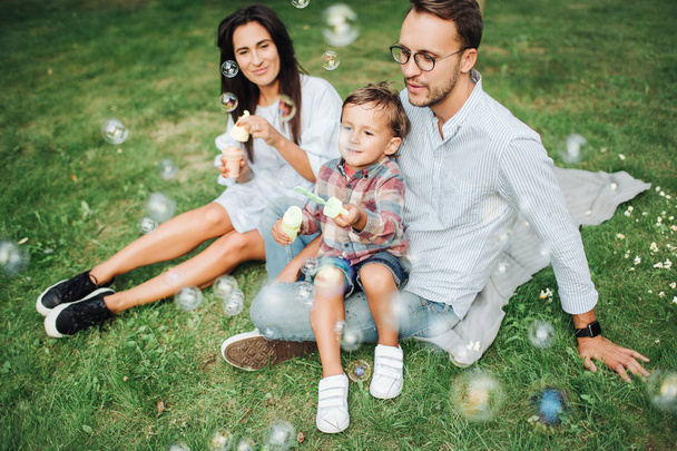 Happy young family playing with bubble wands in park outdoors - Foto, Bild