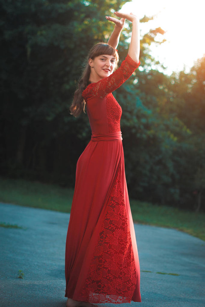 Όμορφη νεαρή κοπέλα σε ένα κόκκινο μακρύ φόρεμα χορού. - Φωτογραφία, εικόνα