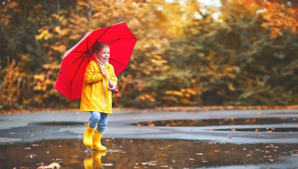 gelukkig kind meisje met een paraplu en rubber laarzen in plas op - Foto, afbeelding