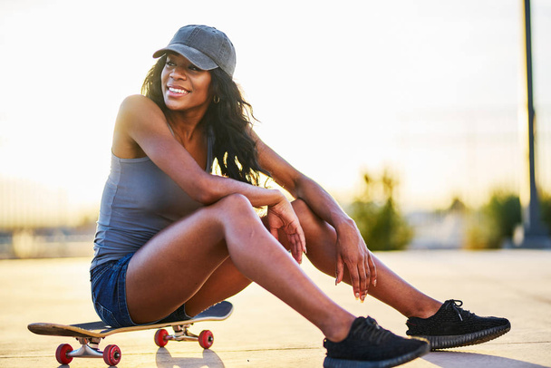 Woman sitting on skateboard while taking selfie against sky - Photo, Image