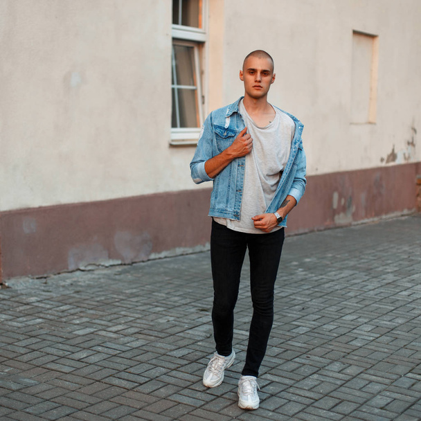 Elegante giovane uomo in giacca di jeans, una t-shirt grigia e jeans neri in scarpe bianche per strada
 - Foto, immagini
