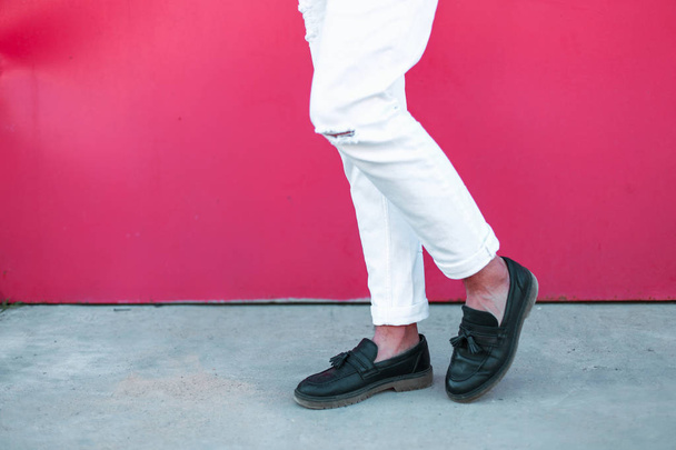 Gambe da uomo con scarpe nere in pelle e pantaloni bianchi vicino a una parete rosa brillante
 - Foto, immagini