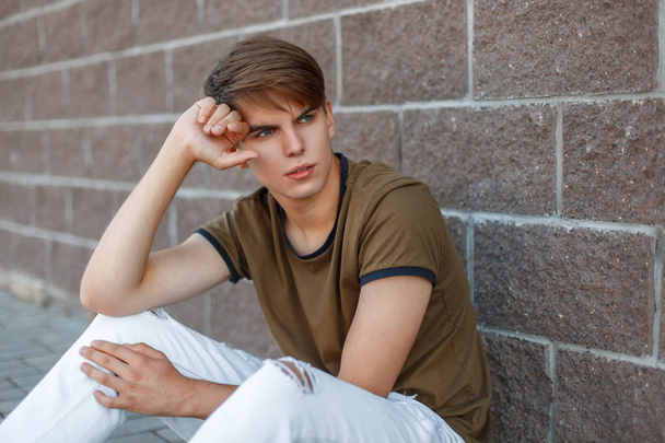 Handsome man with hair sitting near a brick wall - Foto, afbeelding