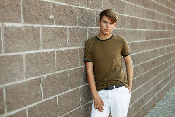 joven hombre de moda en una camiseta y pantalones blancos cerca de una pared de ladrillo
 - Foto, imagen