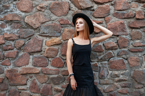 Belle femme élégante en vêtements noirs à la mode avec chapeau près d'un mur de pierre
 - Photo, image