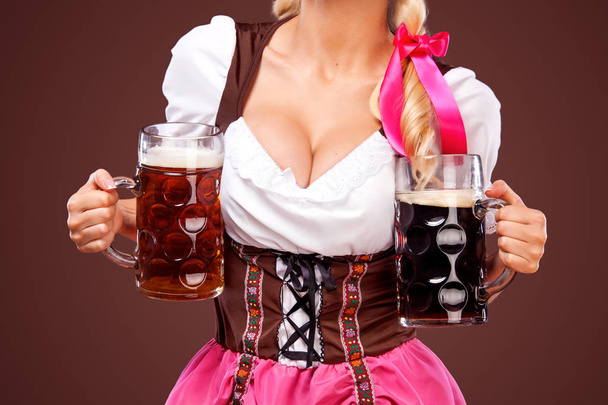 Closeup portrait of boyd Oktoberfest girl - waitress, wearing a traditional Bavarian dress, serving big beer mugs on black background. - Foto, imagen