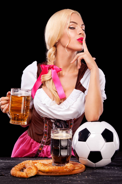 Молода сексуальна Октоберфест дівчина - офіціантка, носіння традиційні баварські плаття, де подають великий пивні кухлі і беручи футбольний м'яч на чорному тлі. - Фото, зображення