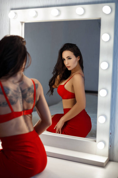 Hermosa joven en ropa interior sexy roja se sienta cerca de un espejo vintage con bombillas
 - Foto, Imagen