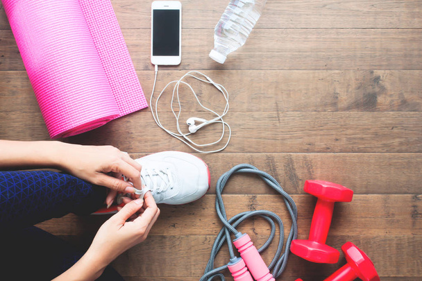 Bovenaanzicht van sport en fitness vrouw koppelverkoop schoenen met mobiele apparaten en uitrusting van de sport op houten vloer - Foto, afbeelding