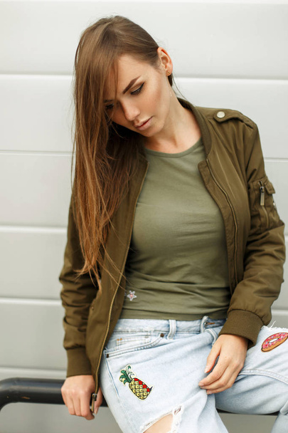 Beautiful young woman with freckles in street style in a jacket and a T-shirt with jeans near a metal wall - Photo, Image