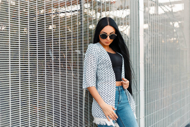 Beautiful young woman in trendy stylish clothes with vintage sunglasses near the grid - Photo, Image