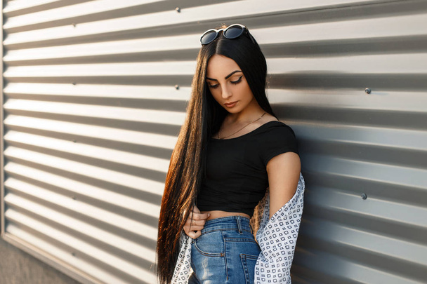 Bella giovane donna con i capelli ben curati in abiti alla moda vicino a un muro di metallo in una giornata di sole
 - Foto, immagini