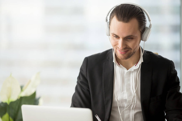 Hombre de negocios sonriente en auriculares mirando la pantalla del ordenador portátil
. - Foto, Imagen