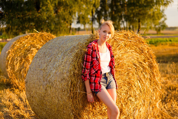junges Mädchen auf Strohgarben auf einem Feld - Foto, Bild
